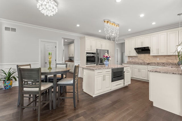 kitchen with under cabinet range hood, visible vents, stainless steel appliances, and a notable chandelier