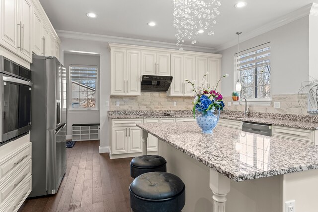 kitchen featuring extractor fan, stainless steel appliances, a sink, ornamental molding, and a kitchen bar