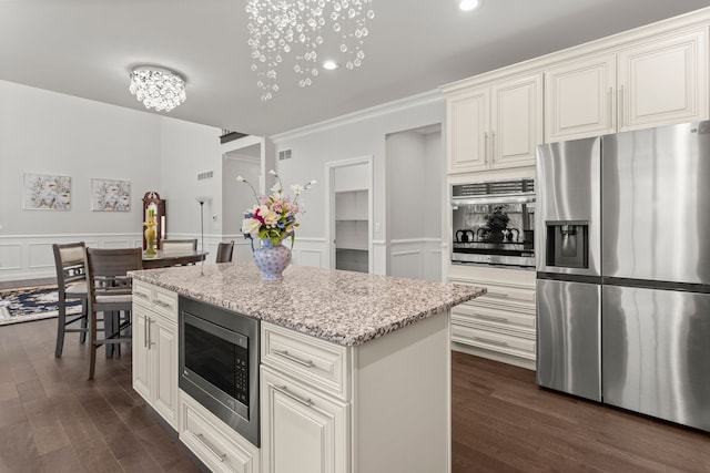 kitchen featuring light stone counters, dark wood-style floors, stainless steel appliances, wainscoting, and a kitchen island