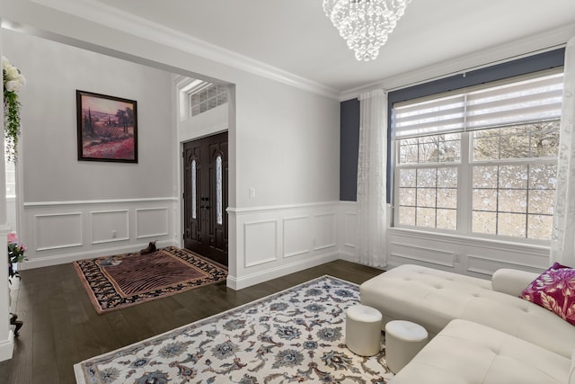 living area featuring ornamental molding, a decorative wall, wood finished floors, and a notable chandelier