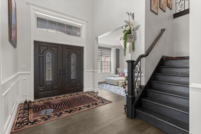 foyer entrance with hardwood / wood-style flooring, a decorative wall, a towering ceiling, stairway, and wainscoting