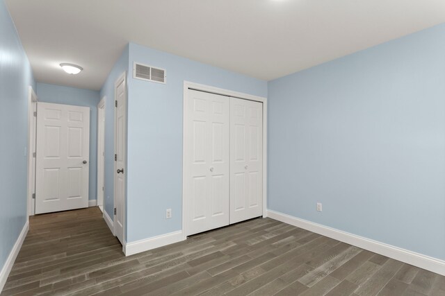 unfurnished bedroom with a closet, visible vents, baseboards, and wood finished floors