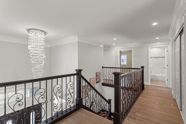 hallway with an inviting chandelier, ornamental molding, wood finished floors, and an upstairs landing