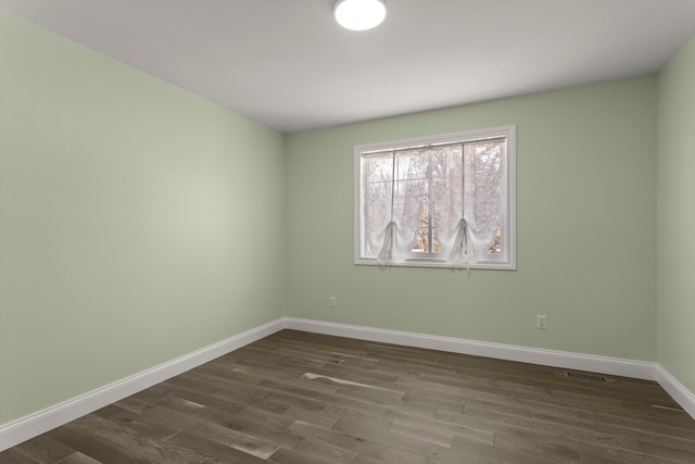 empty room featuring visible vents, baseboards, and dark wood finished floors