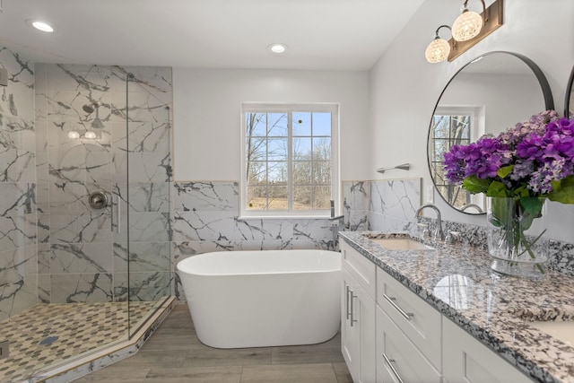 bathroom with double vanity, a marble finish shower, a soaking tub, a sink, and tile walls