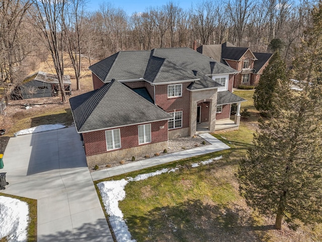 view of front of property featuring driveway, a chimney, roof with shingles, covered porch, and brick siding