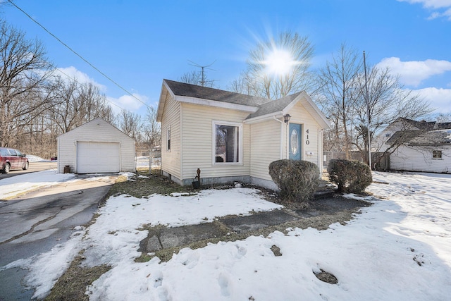 view of snowy exterior with a garage, driveway, fence, and an outbuilding