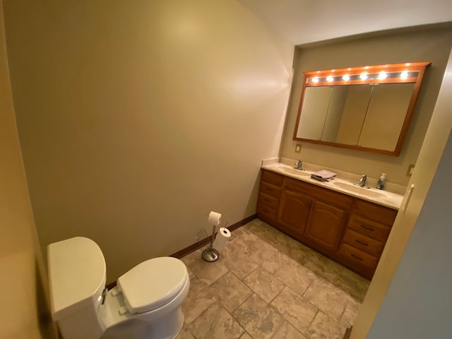 bathroom with toilet, double vanity, baseboards, and a sink