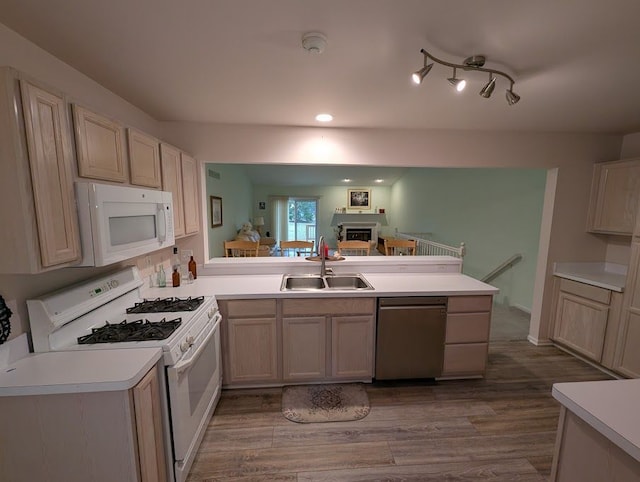 kitchen with a peninsula, white appliances, wood finished floors, a sink, and light countertops