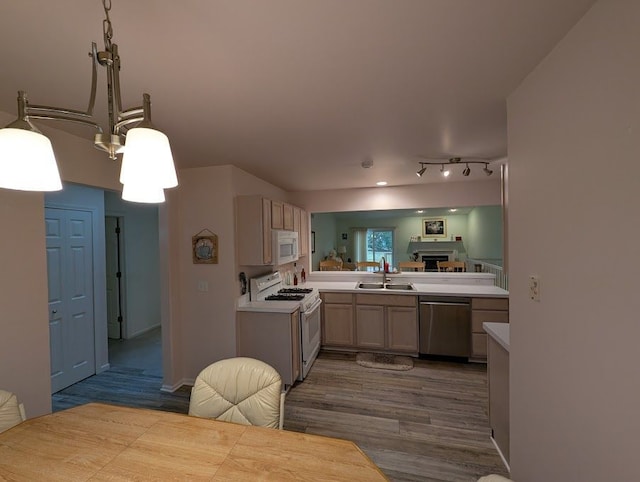 kitchen featuring white appliances, wood finished floors, light countertops, pendant lighting, and a sink