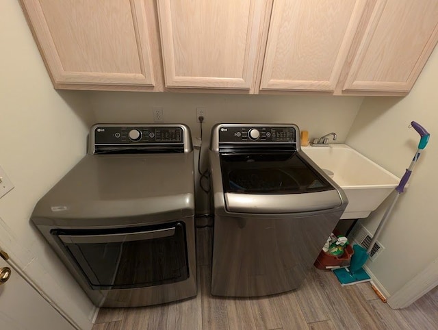 laundry area with a sink, wood finished floors, baseboards, cabinet space, and washer and clothes dryer