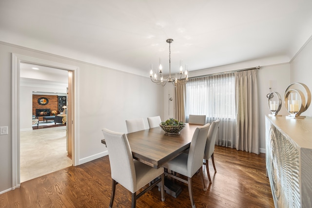 dining room featuring a chandelier, dark wood-type flooring, a brick fireplace, and baseboards