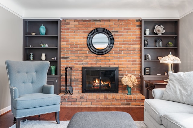 living area with a brick fireplace, baseboards, built in features, and wood finished floors