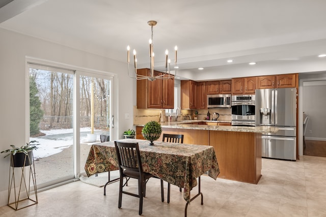 kitchen with light stone counters, stainless steel appliances, a peninsula, brown cabinets, and decorative backsplash