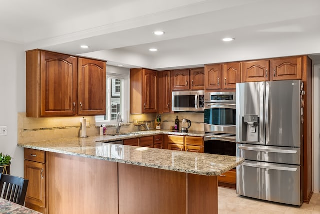 kitchen featuring brown cabinets, decorative backsplash, appliances with stainless steel finishes, light stone countertops, and a peninsula