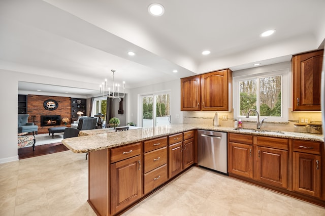 kitchen with dishwasher, light stone counters, a peninsula, a brick fireplace, and a sink