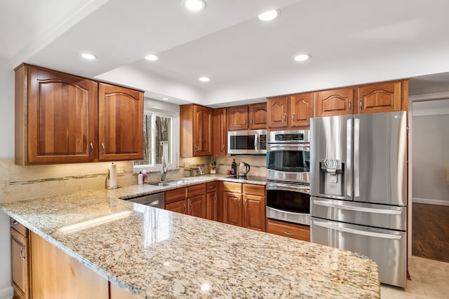 kitchen featuring light stone countertops, appliances with stainless steel finishes, brown cabinetry, and a sink