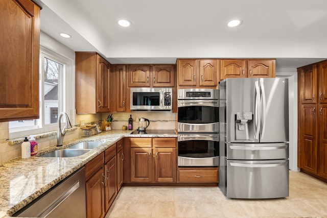 kitchen with appliances with stainless steel finishes, brown cabinetry, a sink, and light stone countertops