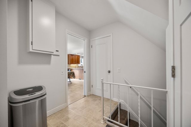 hall featuring baseboards, vaulted ceiling, and an upstairs landing