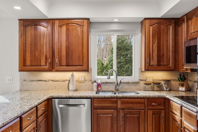 kitchen with light stone counters, recessed lighting, stainless steel appliances, a sink, and backsplash