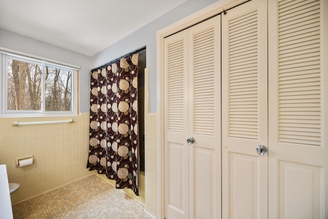 bathroom with tile patterned flooring, a shower with shower curtain, tile walls, a closet, and wainscoting