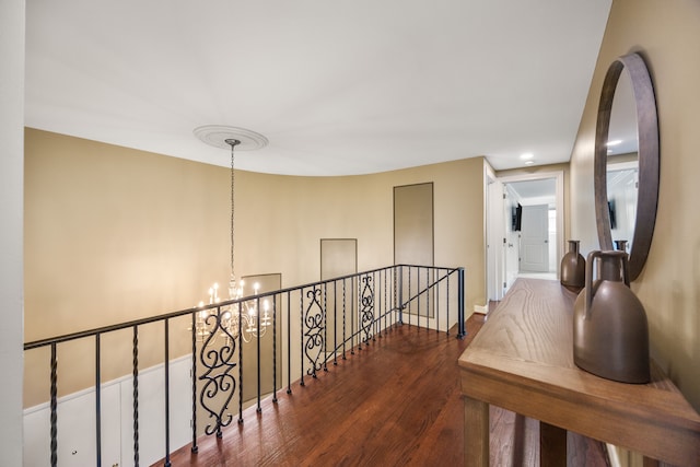 corridor with a chandelier, an upstairs landing, and wood finished floors