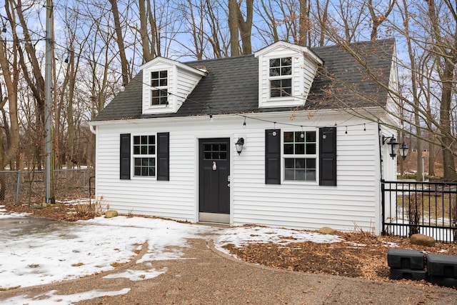 cape cod-style house featuring a shingled roof and fence