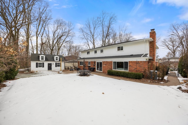 rear view of house featuring an outbuilding, brick siding, a chimney, and fence