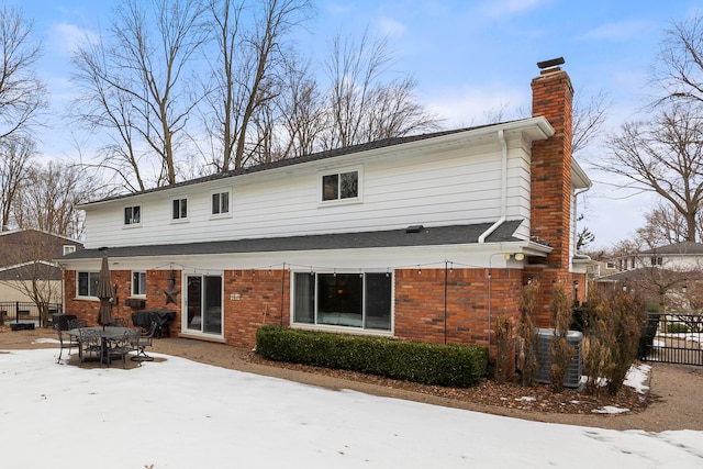 rear view of house featuring brick siding, a chimney, central AC unit, and fence