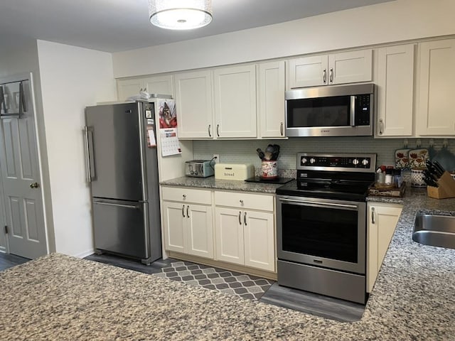 kitchen with appliances with stainless steel finishes, stone counters, white cabinets, and decorative backsplash