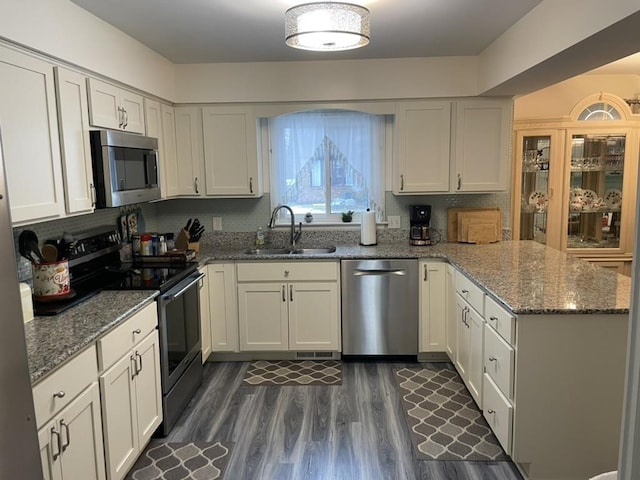 kitchen with appliances with stainless steel finishes, white cabinets, a sink, and a peninsula