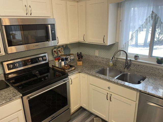 kitchen with tasteful backsplash, appliances with stainless steel finishes, white cabinetry, a sink, and light stone countertops