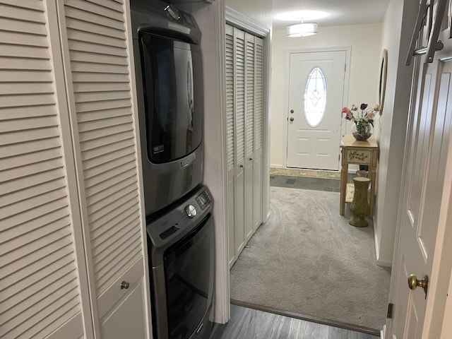 laundry area with carpet floors, stacked washer and dryer, laundry area, and wood finished floors