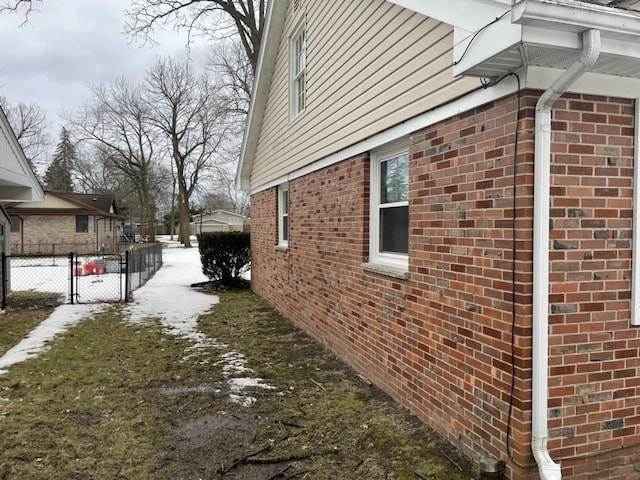 view of side of home with a gate, brick siding, and fence