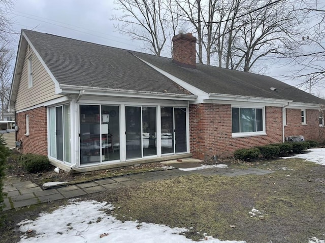 view of front of home featuring a shingled roof, a sunroom, brick siding, and a chimney