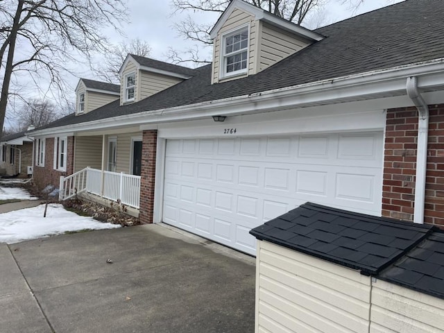 view of side of property with a garage, brick siding, a shingled roof, and aphalt driveway