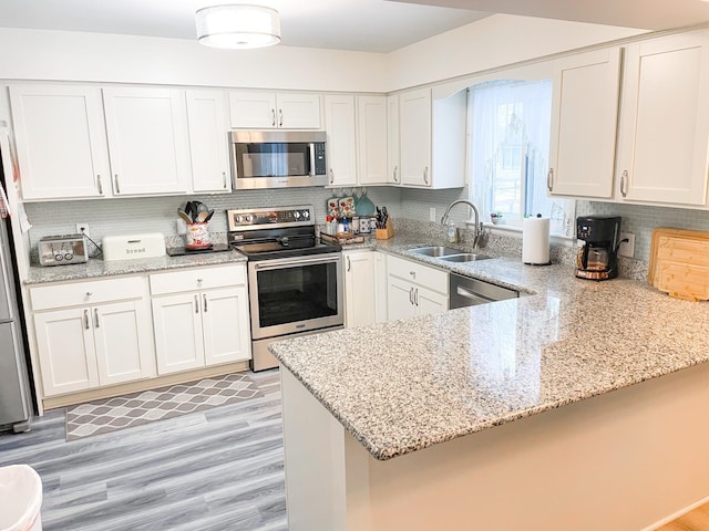 kitchen featuring stainless steel appliances, a peninsula, a sink, white cabinetry, and tasteful backsplash