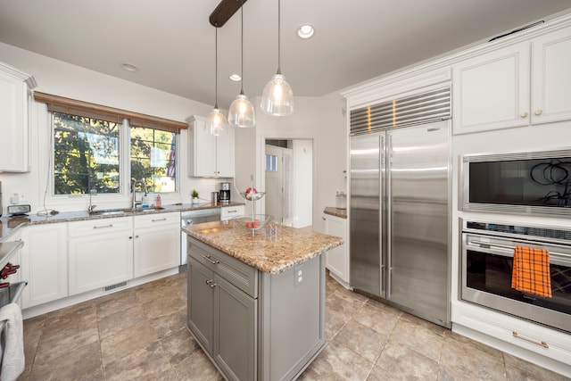 kitchen with visible vents, white cabinetry, a sink, light stone countertops, and built in appliances