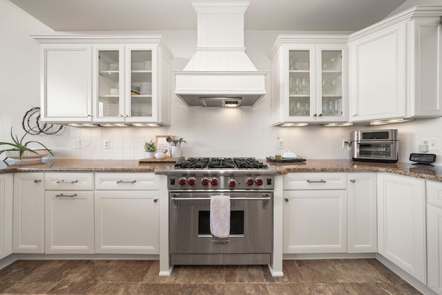 kitchen featuring premium range hood, premium stove, white cabinetry, and tasteful backsplash