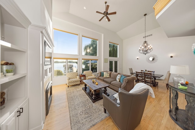 living area with ceiling fan with notable chandelier, high vaulted ceiling, light wood-type flooring, and visible vents