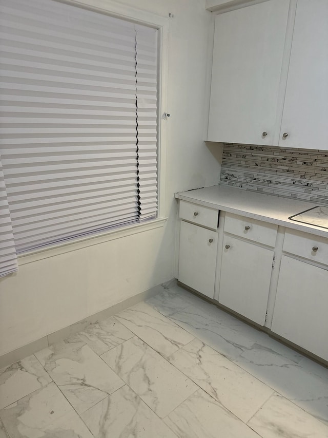 kitchen with marble finish floor, light countertops, decorative backsplash, white cabinetry, and baseboards