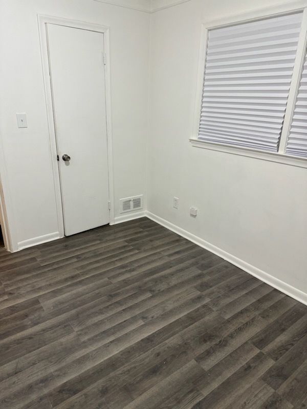 empty room featuring dark wood-style floors, baseboards, and visible vents