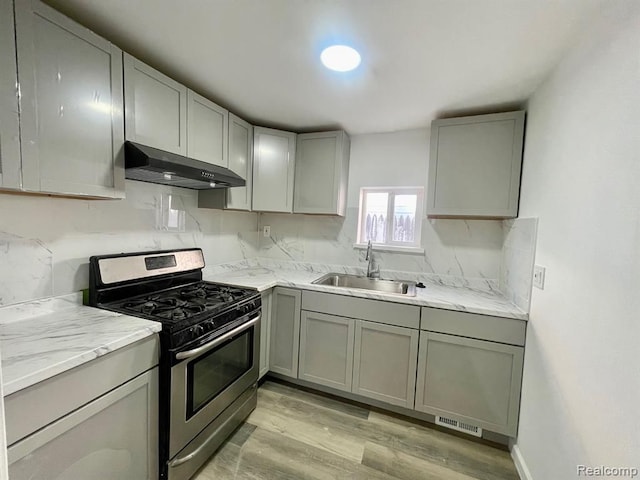 kitchen featuring gray cabinets, a sink, gas range, and under cabinet range hood