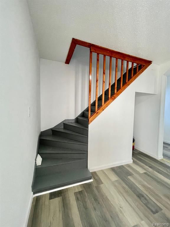 stairway with a textured ceiling, baseboards, and wood finished floors