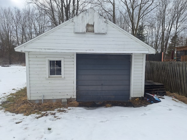 snow covered garage featuring fence and a detached garage