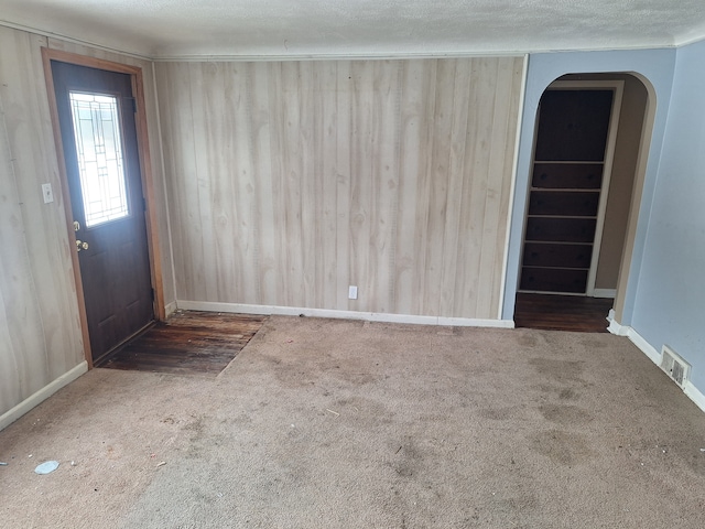 empty room featuring arched walkways, a textured ceiling, carpet flooring, visible vents, and baseboards