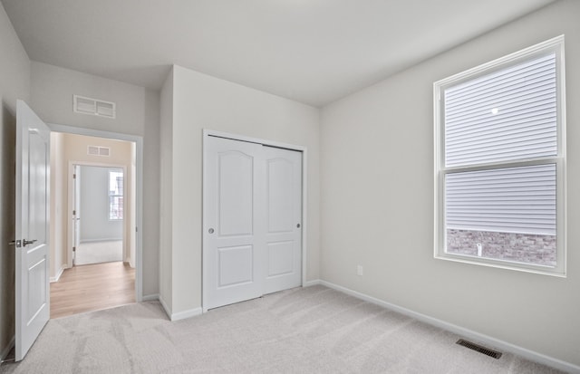 unfurnished bedroom featuring visible vents, a closet, and light colored carpet