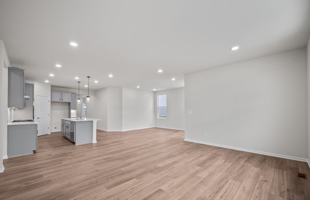 unfurnished living room with light wood finished floors, baseboards, a sink, and recessed lighting