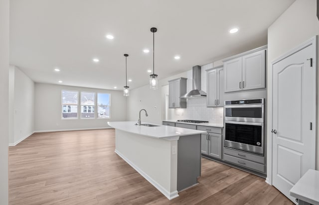 kitchen with wall chimney range hood, stainless steel double oven, a sink, and gray cabinets