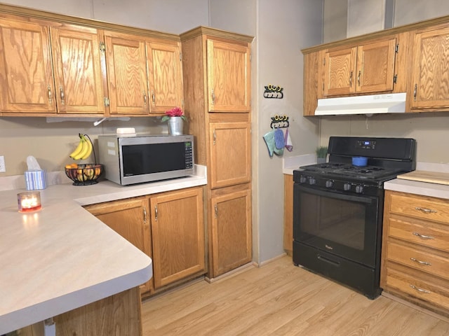 kitchen featuring brown cabinetry, black gas range oven, stainless steel microwave, light countertops, and under cabinet range hood